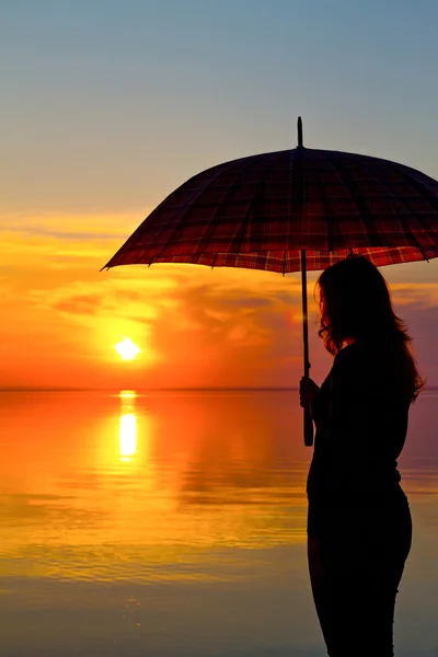 Silhouette di una ragazza con un ombrellone al tramonto sulla spiaggia — Foto Stock