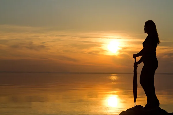 Silueta de una chica con un paraguas en la puesta de sol en la playa —  Fotos de Stock