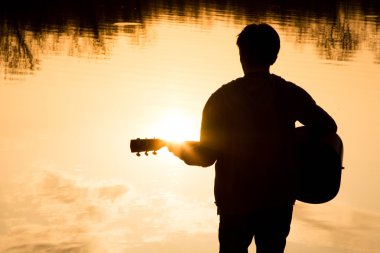 genç bir adam sahilde gitar silüeti