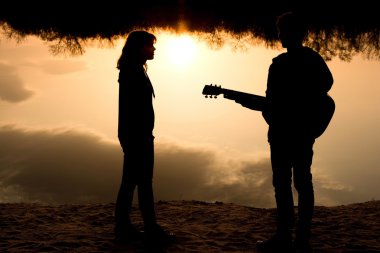 siluet bir genç erkek ve kız sahilde gitar