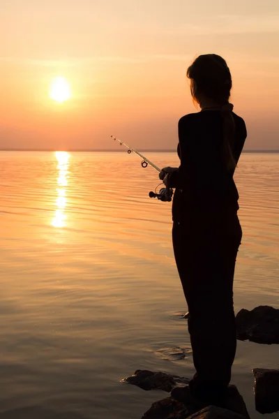 Silhouette of a girl on the bank of the river with a fishing rod — Stock Photo, Image