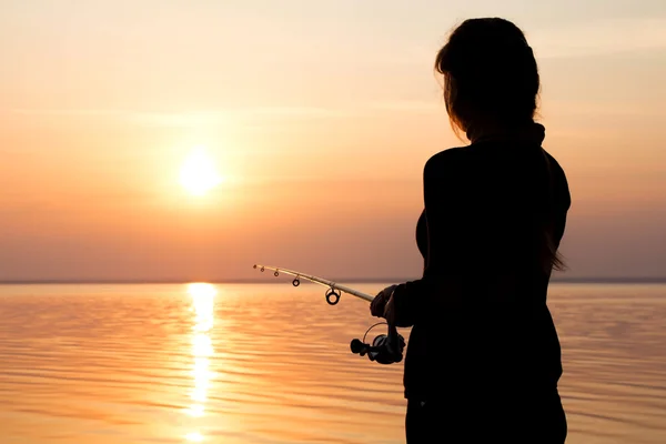 Silhouette di una ragazza sulla riva del fiume con una canna da pesca — Foto Stock