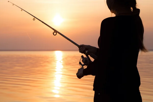 Giovane ragazza pesca al tramonto vicino al mare — Foto Stock