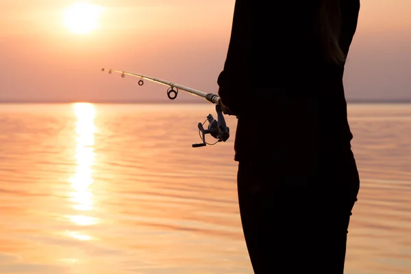 Silhouette di una ragazza sulla riva del fiume con una canna da pesca — Foto Stock