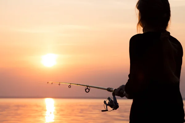 Giovane ragazza pesca al tramonto vicino al mare — Foto Stock