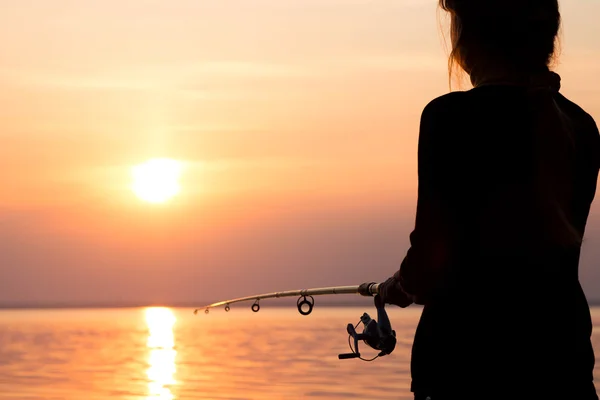 Silhouette di una ragazza sulla riva del fiume con una canna da pesca — Foto Stock