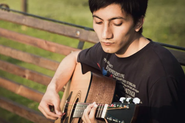 Kleiner Junge spielt Gitarre auf einer Bank — Stockfoto