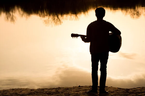 Silhouette eines jungen Mannes am Strand mit einer Gitarre — Stockfoto