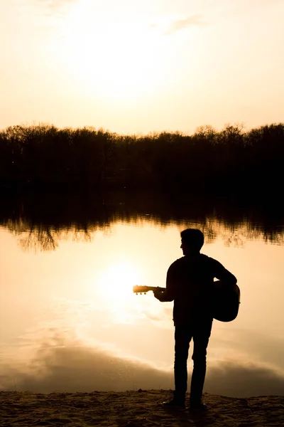 Sylwetka młodego człowieka na plaży z gitarą — Zdjęcie stockowe