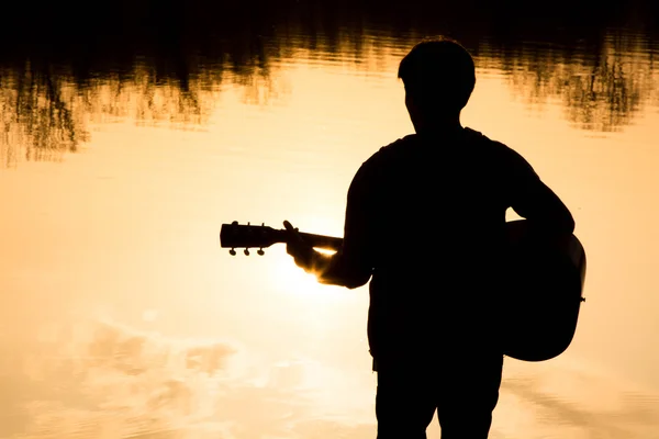 Silhouette eines jungen Mannes am Strand mit einer Gitarre — Stockfoto