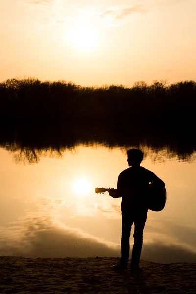Silhouette eines jungen Mannes am Strand mit einer Gitarre — Stockfoto