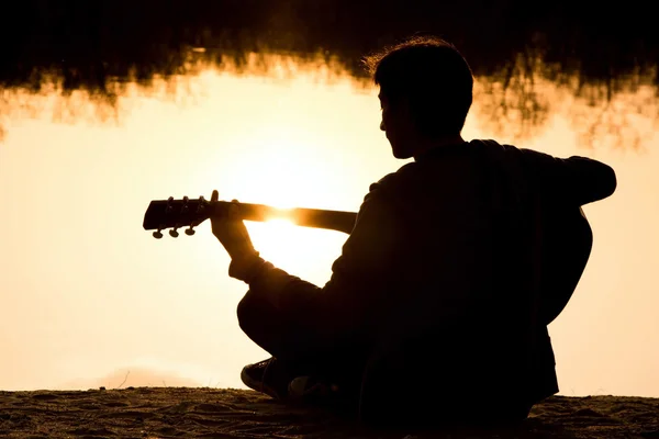 Silhuetten av en ung man på stranden med en gitarr — Stockfoto