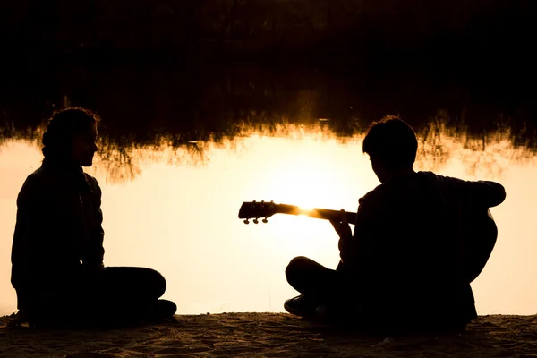 Silhouette of a young boy and girl on the beach with a guitar — Stock Photo, Image