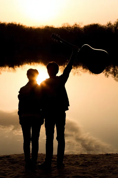 Silhouette eines Jungen und eines Mädchens am Strand mit einer Gitarre — Stockfoto