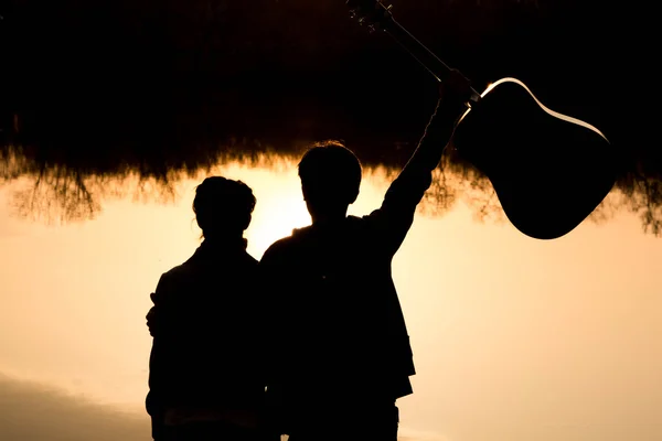 Sylwetka młody chłopak i dziewczyna na plaży z gitarą — Zdjęcie stockowe