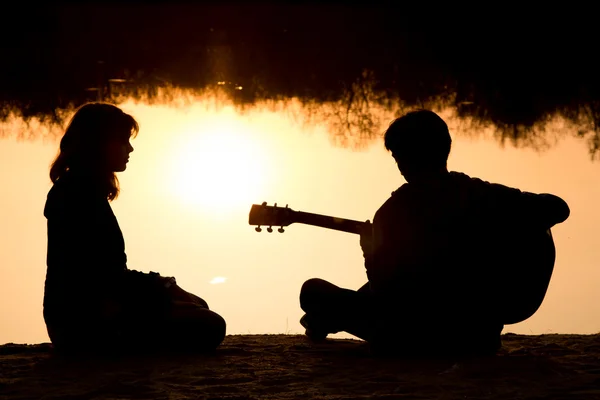 Silhueta de um menino e menina na praia com uma guitarra — Fotografia de Stock