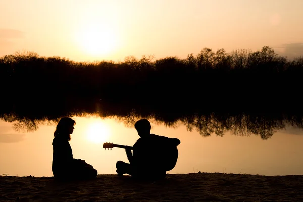 Silhouette d'un jeune garçon et d'une jeune fille sur la plage avec une guitare — Photo