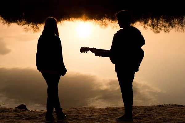 Silhouette eines Jungen und eines Mädchens am Strand mit einer Gitarre — Stockfoto