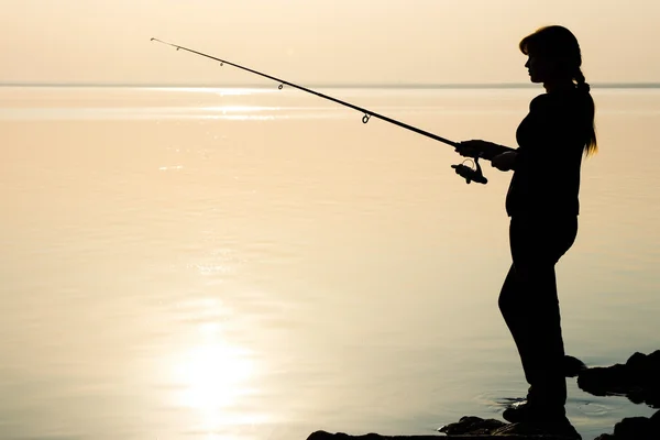 Silhouette of a young girl fishing at sunset near the sea — Stock Photo, Image