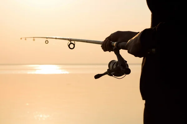 Silhouette da pescatore al tramonto vicino al mare con una canna da pesca — Foto Stock