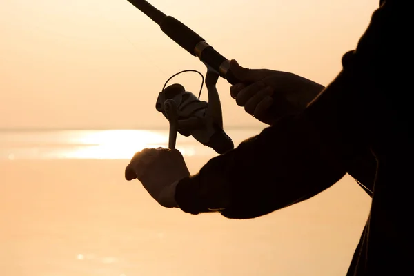 Silhouette da pescatore al tramonto vicino al mare con una canna da pesca — Foto Stock