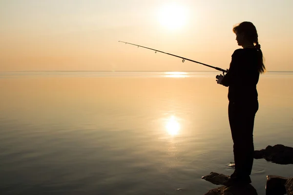 Silhouette eines jungen Mädchens beim Angeln bei Sonnenuntergang am Meer — Stockfoto