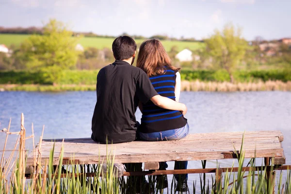 Homem abraça menina sentado em um cais na margem do rio — Fotografia de Stock