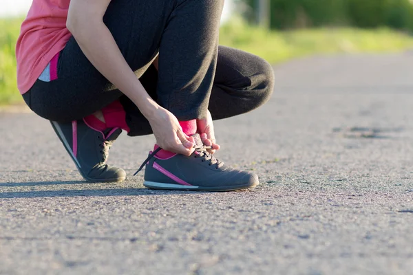 Chica atando zapatos de cordones de zapatos sentado en el camino de asfalto — Foto de Stock