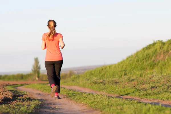 Menina em um terno esportivo corre ao longo do campo — Fotografia de Stock