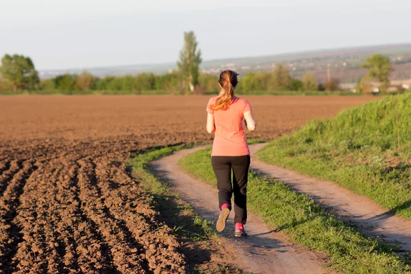 Dziewczyna w komplet sportowych biegnie wzdłuż pola — Zdjęcie stockowe