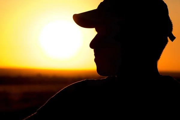 Silhueta de um jovem em um campo ao pôr do sol — Fotografia de Stock