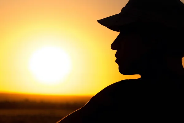 Silhueta de um jovem em um campo ao pôr do sol — Fotografia de Stock