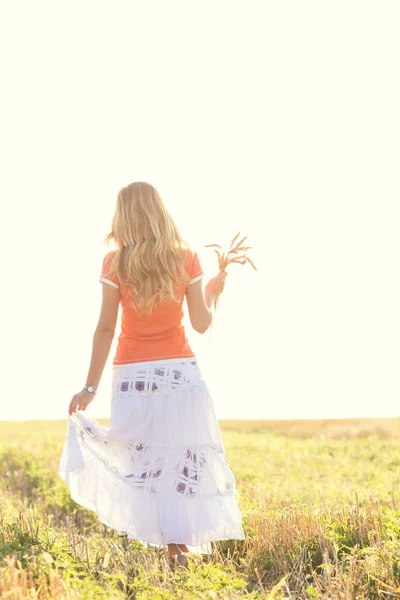 Молодая девушка идет в поле с ушами в руке — стоковое фото