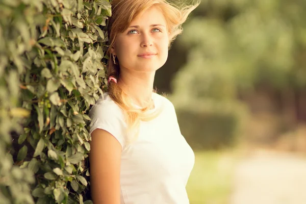 Retrato de uma bela mulher em pé perto de um arbusto verde — Fotografia de Stock