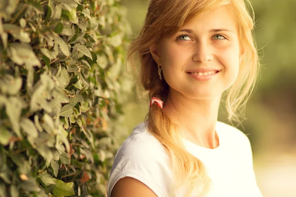 Portrait of a beautiful woman standing near a green bush — Stock Photo, Image