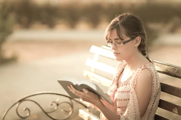 Young girl with book in hand on a bench — Stock Photo, Image