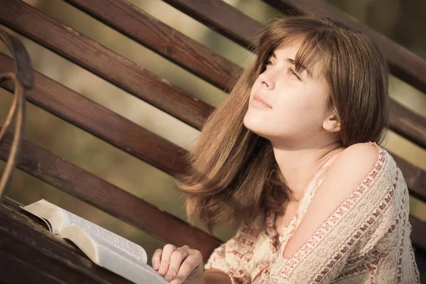 Mujer leyendo un libro tumbado en el banco — Foto de Stock