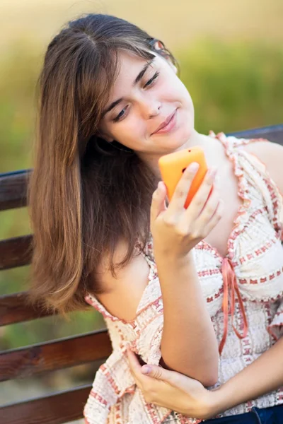 Młoda piękna kobieta z telefonem na ławce w parku — Zdjęcie stockowe