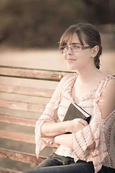 Vrouw in glazen met een boek op een bankje — Stockfoto