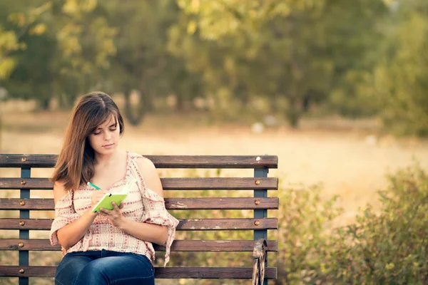 Chica joven con cuaderno en un banco — Foto de Stock