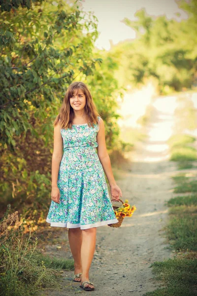 Beautiful girl with a basket of flowers on a walk — Stock Photo, Image