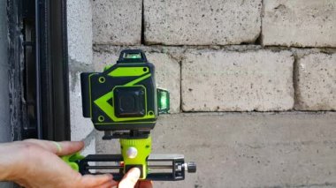 Evin duvarları duvarlı bir evin açık hava inşaatı için inşaat alanındaki yeşil ışığı ölçmek için lazer seviyesinde gösterge. Konut binalarının inşaatı. Mimarlık ve tasarım. İnsan elleri duvardaki lazer ışınını ayarlar..