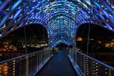 Gürcistan 'ın Tiflis kentindeki yaya köprüsü (Barış Köprüsü) gece vakti Kura Nehri üzerinde camla kaplanmış aydınlık çelik bir çerçeveyle.
