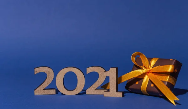 2021 yazıtları ve üzerinde puantiyeli renkli kağıtlar olan hediye kutusu mavi arka planda sarı kurdele ile bağlanmış. Noel ve Yeni Yıl kartı, afiş, reklam konsepti. 