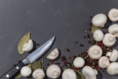 Siyah taş arka planda mantar ve baharatlar. Siyah, kırmızı, beyaz biber, defne yaprağı ve karanfil. Bıçak ve kesilmiş mantar. Kopyalama alanı, üst görünüm. 