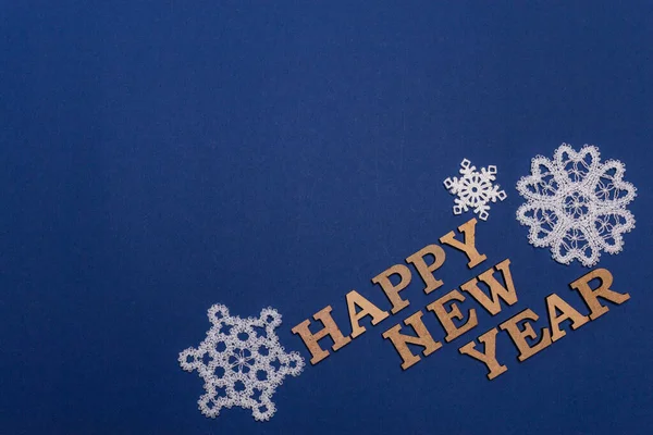 White snowflakes on blue background. Inscription Happy New Year. Christmas and New Year card, banner, advertising concept. Top view photo, minimalism, copy space. Medical flatly. — Stock Photo, Image