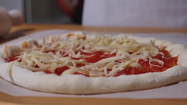 Las manos están echando queso rallado en la masa de pizza. Pizza casera de queso con salsa de tomate. Preparar la tradicional pizza italiana en casa. Primer plano de vídeo. — Vídeos de Stock