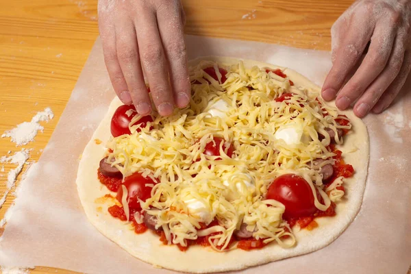 Ahşap masadaki fırın kağıdında çiğ pizza. Domates soslu, domates kirazlı, sosisli ve hamurlu ev yapımı peynirli pizza hazırlıyorum. Yüksek kalite fotoğraf