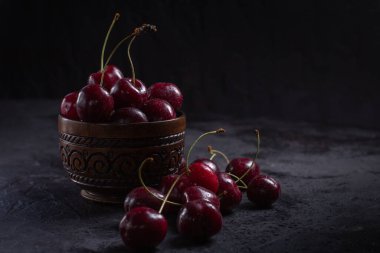 Arka planda böğürtlenlerin üzerine su damlatılan bir kasede organik sulu kiraz. Yakın plan fotoğraf, sade tuş. 