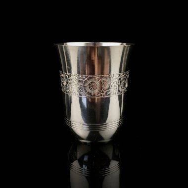 Siyah arkaplanda grafikleri olan antika metal shot bardağı.